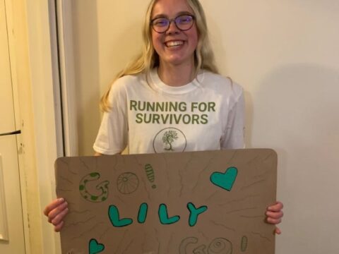 A young woman with blonde hair holds up a sign that says, 